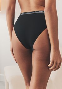 Ropa interior negra de algodón de talle alto con una cinturilla elástica con la marca, que presenta una textura suave y un diseño minimalista.