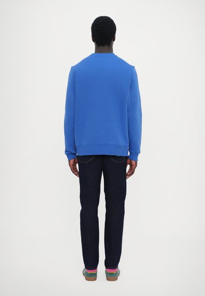 Sweat-shirt en coton bleu avec un col ras du cou, associé à un jean en denim foncé et des chaussures multicolores, vu de dos.
