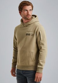 Beige Kapuzenpullover aus weicherm Stoff mit einer Fronttasche und gerippten Bündchen. Enthält bedruckte Logodetails auf der Brust und dem linken Ärmel.