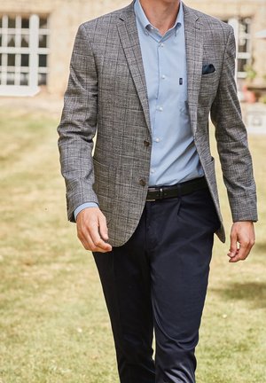 Harmaa ruudullinen bleiseri vaaleansinisen napitettavan kauluspaidan päällä, yhdistetty tummansinisiin housuihin ja mustaan vyöhön. Taskuliina lisää kontrastia asuun.