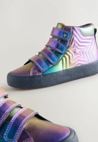 Holografikus fényű, magas szárú sneaker, három tépőzáras pánttal, texturált gumitalppal és csillagmintás díszítésekkel.