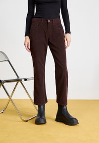 Pantalones de pana marrones con corte recto, bolsillos frontales y cierre de un solo botón, combinados con botas de tobillo negras y gruesas.