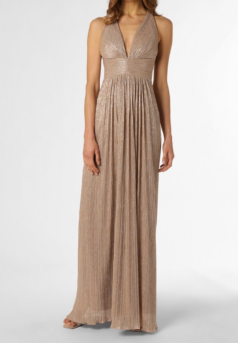 Robe plissée sans manches en or métallisé avec un profond décolleté en V et une taille cintrée, portée avec des talons ouverts, sur fond neutre.