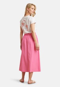 Weißes T-Shirt mit Palmen-Graphic, kombiniert mit einem fließenden pinken Maxikleid. Der Rock hat einen elastischen Bund und eine glatte Textur.