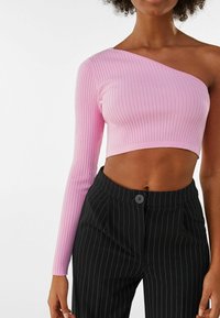 Top asimétrico recortado en tejido de rayas de color rosa con una manga larga; combinado con pantalones de pinzas negros de cintura alta que cuentan con un cierre de botón.