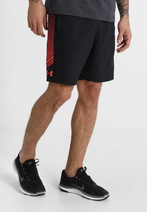 Mann in schwarzen Sportshorts mit roten Einsätzen und Logo an den Seiten, schwarzen Nike-Laufschuhen, stehend auf einer weißen Oberfläche.