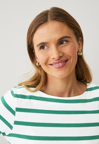 Witte en groene gestreepte shirt met een bootneklijn; gladde stof; gecombineerd met gouden creolen; subtiele textuur.
