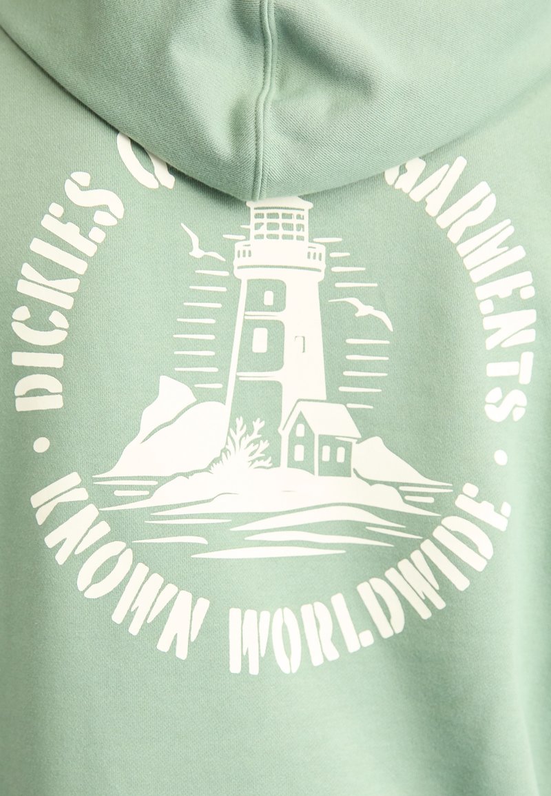 Mint green hoodie featuring a white lighthouse graphic surrounded by text. Smooth texture with a relaxed hood design and subtle ocean scene.