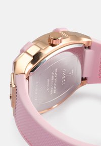 Pink silicone watch with a textured strap, rose gold case, and crown. The back features engraved brand details and a smooth metal finish.