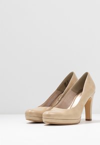 Décolleté in pelle verniciata beige con una superficie liscia, punta rotonda, piattaforma anteriore e alto tacco a stiletto. Design semplice e forma elegante.