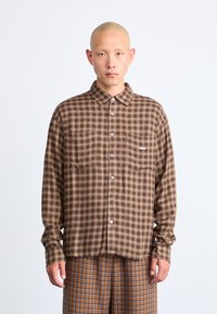 Brown and beige checked shirt with long sleeves, two chest pockets, and buttons. Features an embroidered logo on the left pocket.