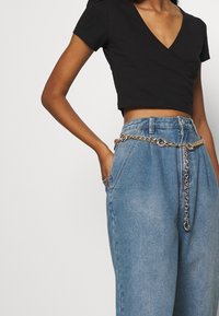 Un top court croisé noir associé à un pantalon en denim bleu clair taille haute, orné d'une ceinture en chaîne argentée pour plus de détails.