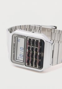 Digitalur med en rektangulær sølvkapsel, en metallrem og et sort knappanel. Skærmen viser tid og forskellige indstillinger i kraftige farver.