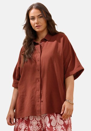 Camisa holgada de color óxido, con botones, hecha de lino texturizado, que presenta un cuello y mangas enrolladas, combinada con pantalones estampados.