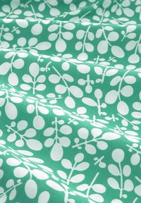 Grüner Stoff mit einem sich wiederholenden Muster aus weißen Blättern und Stängeln, mit einer glatten Textur und geschichteten Falten, die Tiefe schaffen.