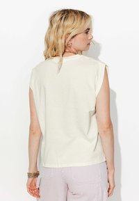Débardeur crème sans manches avec une coupe décontractée, en tissu doux, et coutures d'épaule roulées, associée à un pantalon léger à rayures.
