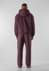 Lilla hættebluse og matchende sweatpants, lavet af blødt stof. Har en stor hætte, ribbede manchetter og en afslappet pasform.