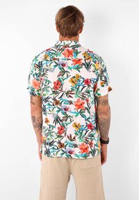 Chemise à manches courtes, avec col, présentant un motif floral aux couleurs vives sur un fond rose clair. Fabriquée en tissu léger.