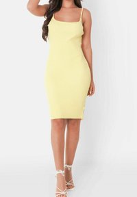 Robe midi jaune à côtes avec fines bretelles et fente sur le côté, associée à des talons blancs à lanières. Texture lisse et silhouette ajustée.