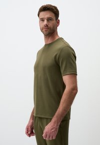 T-shirt verde oliva a maniche corte realizzato in morbido tessuto, con scollatura rotonda e vestibilità comoda, abbinato a pantaloni coordinati.
