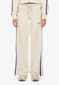 Crème kleurige sweatpants met een relaxte pasvorm, voorzien van marineblauwe zijstrepen en "Superdry" borduursel op de linker dij. Koord in de taille.