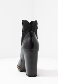 Zwarte enkellaars met hak, gemaakt van glad leer en zacht zwart suède, met een afgeronde neus en een textuurdetail op de hak.