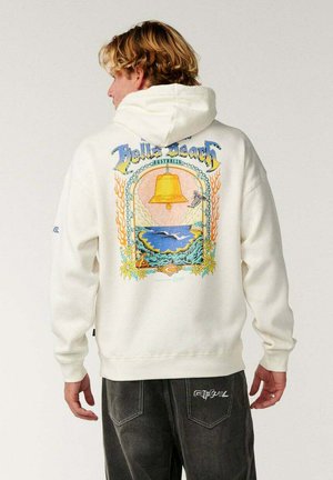 Giovane con capelli biondi che indossa una felpa con cappuccio bianca con un design colorato di Bells Beach Australia con una campana e una scena oceanica sul retro.