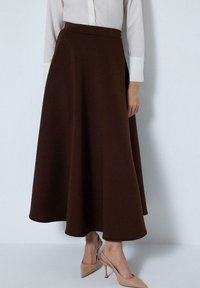 Brown A-line skirt made of smooth fabric, featuring a high waistband and a flowy hemline. Paired with beige pointed-toe heels.