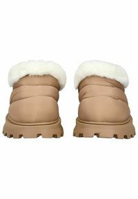 Tan polstrede slip-on sko med en hvid kunstpels krave og en robust beige gummisål. Har en rund tå og quiltet tekstur.