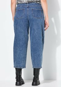 Džínové kalhoty s vysokým pasem a širokými nohavicemi v středně modré barvě, se dvěma zadními kapsami a ohrnutým lemem, doplněné černými kotníkovými botami.