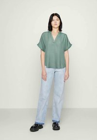 Light green short-sleeve top with a V-neckline, worn with light blue straight-leg jeans and black chunky shoes. Smooth fabric and relaxed fit.
