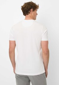 T-shirt bianco a maniche corte con scollo rotondo e texture liscia, caratterizzato da un design semplice e privo di loghi o motivi visibili.