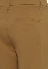 Beige bikses ar izšūtu aizmugures kabatu un gludu auduma faktūru, ar pieguļošu dizainu un minimālām šuvēm, nodrošinot tīru izskatu.