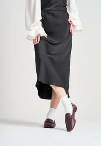Falda de satén negra con dobladillo en forma de cueva, combinada con una blusa blanca y mocasines de cuero burdeos sobre calcetines blancos con volantes.