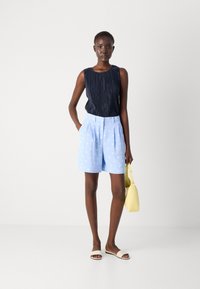 Navy pleated sleeveless top paired with light blue shorts featuring white polka dots, complemented by a yellow bag and slide sandals.
