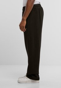 Sorte sweatpants med elastisk talje, sidelommer og en diskret logo detalje. Stoffet er blødt og glat, hvilket giver en afslappet pasform.