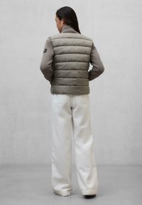 Giubbotto imbottito con parte frontale trapuntata beige e maniche in maglia grigia, abbinato a pantaloni bianchi a gamba larga. Design semplice, senza motivi visibili.