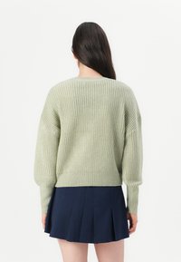 Zielony sweter na drutach o luźnym kroju, z prążkowaną fakturą i długimi rękawami, zestawiony z plisowaną granatową spódnicą.