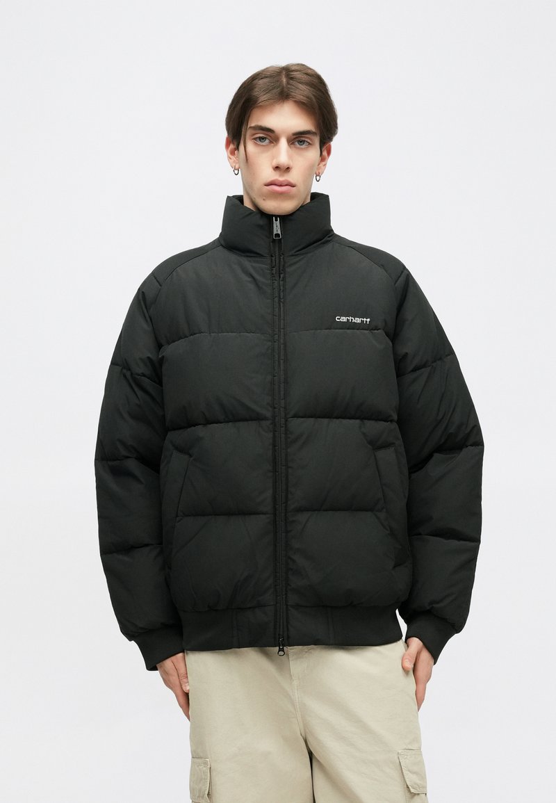 Giacca a vento nera con colletto alto, design a trapunta, zip frontale e accento con logo. Il materiale sembra liscio e isolato, con polsini aderenti.