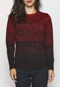 Strickpullover mit Farbverlauf von Rot zu Schwarz, strukturiertem Stoff und geripptem Saum. Kombiniert mit einer schwarzen Hose.