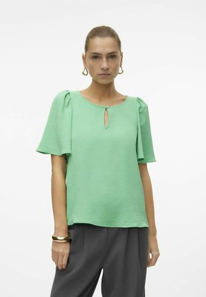Korte mouwen groene blouse met een gestructureerde afwerking, een ronde hals en een sleutelgatdetail. Gepaard met losse grijze broeken.
