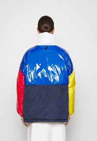 Padded jacket with a shiny blue top, red sleeves, yellow accents, and a navy bottom. High collar and subtle logo at the back.