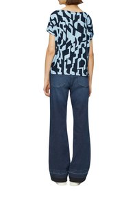 Korte mouwen, gebloemd shirt in lichtblauw en donkerblauw, gecombineerd met uitlopende donkerdenim jeans. De jeans hebben een omgeslagen zoom en achterzakken.