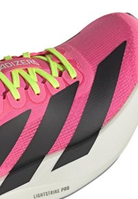 Pink synthetic upper with black accents, featuring bright yellow laces. Lightweight cushioned sole labeled "LIGHTSTRIKE PRO." Sleek design.
