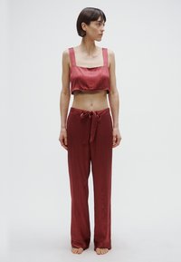 Sarkana satīna divdaļīgs mājokļu komplekts ar kultūraugu topu ar kvadrātveida kakla izgriezumu un vaļīgām biksēm ar jostas saišķi un polka punktu rakstu.