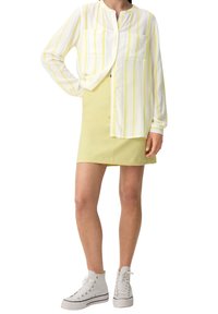 Camicia bianca con strisce verticali gialle, due tasche sul petto; abbinata a una gonna gialla e scarpe alte bianche.