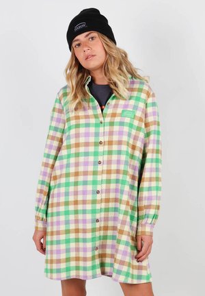 Robe chemise à carreaux multicolores en vert, marron, violet et blanc. Elle présente des manches longues, un bouton sur le devant, et une petite étiquette sur la poitrine.