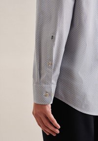 Camicia a maniche lunghe con motivo in azzurro chiaro e piccoli disegni geometrici. Presenta polsini con bottoni e una trama di tessuto liscia.
