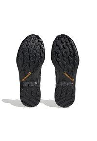 Suelas de calzado atlético negro con un patrón de banda de rodadura multidireccional profundo. Presenta la marca "Continental" en naranja y el logotipo de "adidas" impreso.