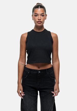 Top noir cropped sans manches avec un décolleté ras du cou, associé à un jean noir taille haute avec des coutures visibles et des coutures latérales.